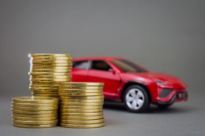 Photo of a stack of coins in front of a red car