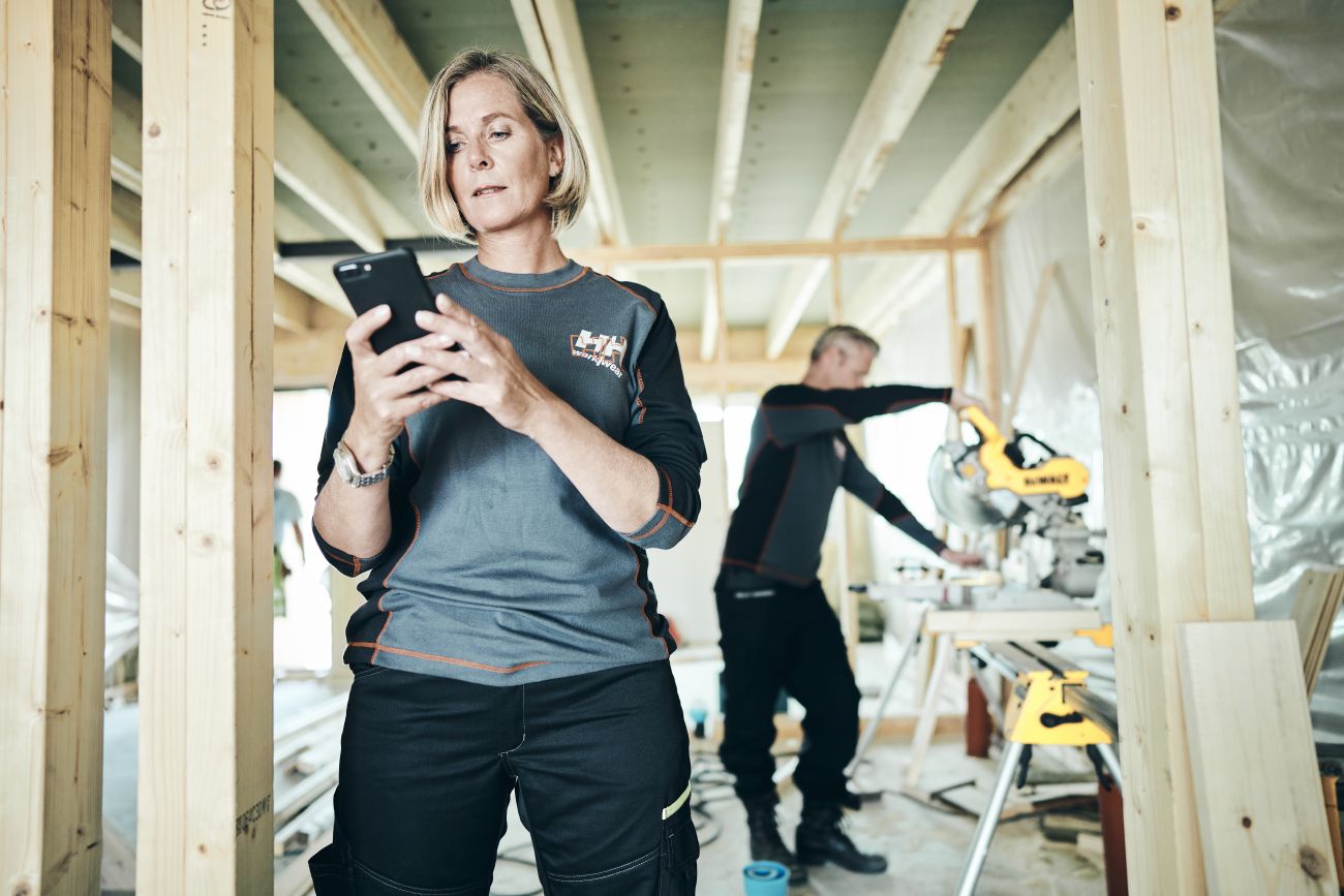 Na zdjęciu dwie osoby pracujące w branży budowlanej, na pierwszym planie kobieta sprawdza telefon