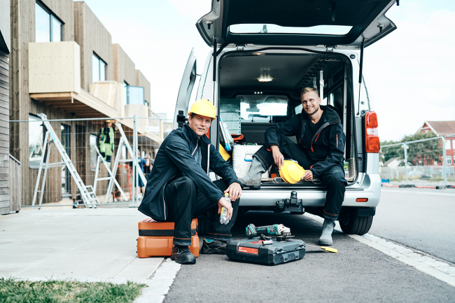 Two workers in a van with tools and hard hats